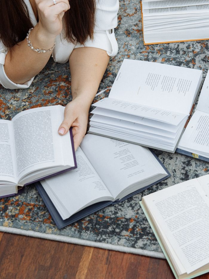 A woman reading multiple books on a carpeted floor, capturing a cozy study environment.