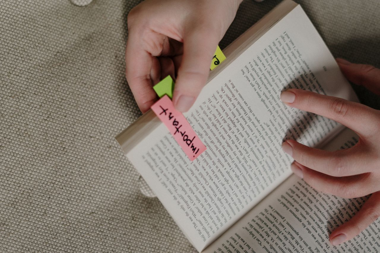 about-us A close-up image of hands marking a book with colorful sticky notes for emphasis.